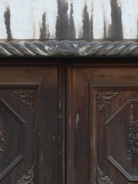 Worn dark brown wooden door with intricately-designed trim and dome-shaped crown.